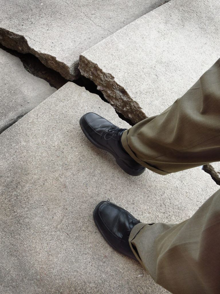Man walking on broken dangerous cracked sidewalk